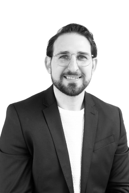 Business professional with glasses and beard smiling in a suit.