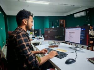 Software developer working at multiple monitors in a modern office.