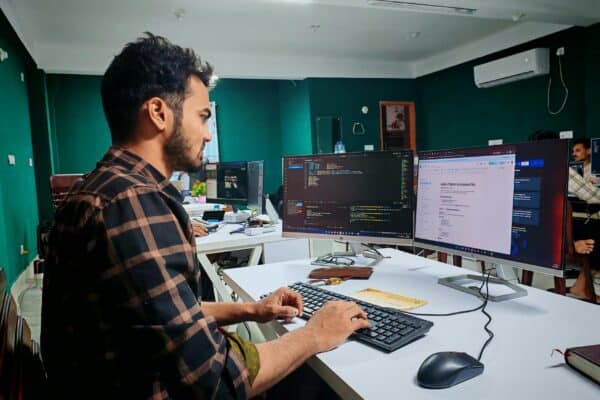 Software developer working at multiple monitors in a modern office.