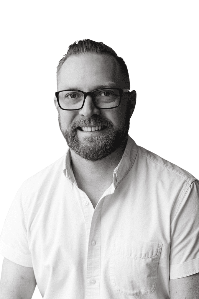 Professional portrait of a man with glasses and beard, smiling, in black and white.