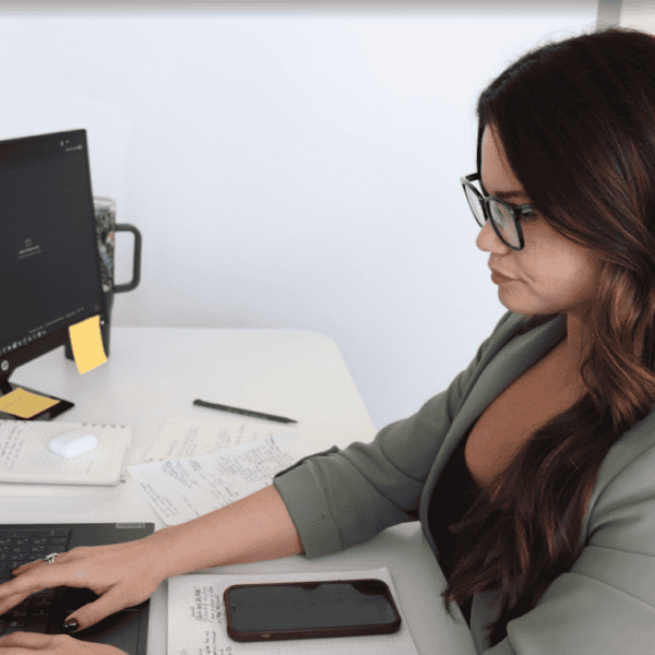 Woman working on computer with coding and notes on desk.