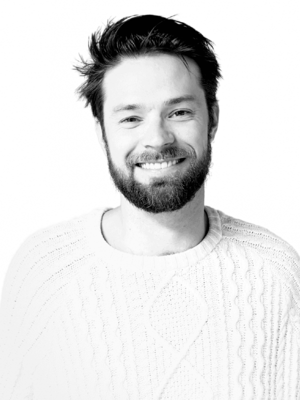 Smiling man with beard in a white sweater, professional headshot.