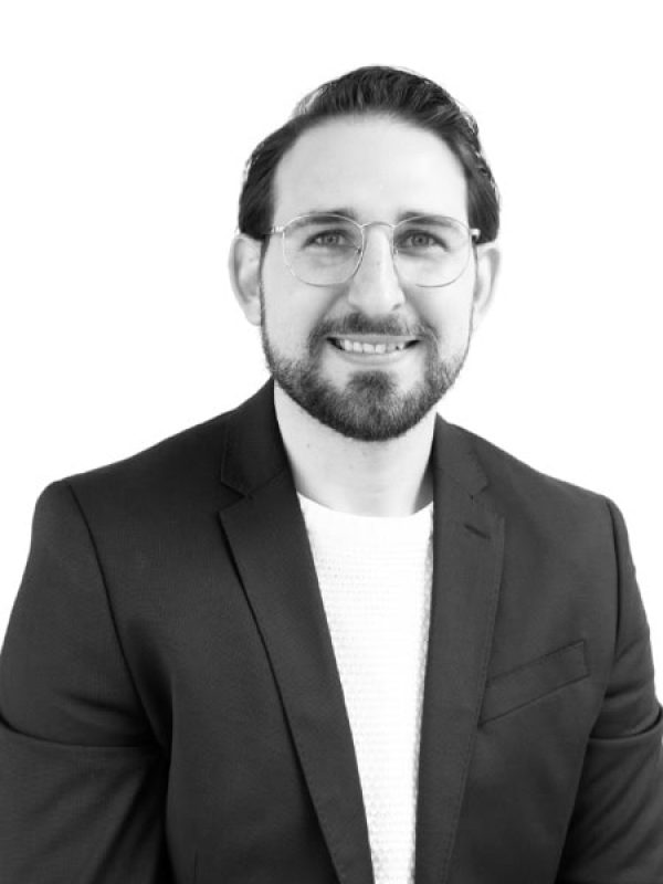 Business professional with glasses and beard smiling in a suit.