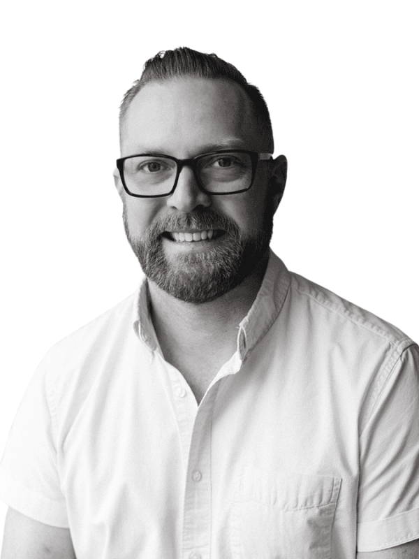 Professional portrait of a man with glasses and beard, smiling, in black and white.